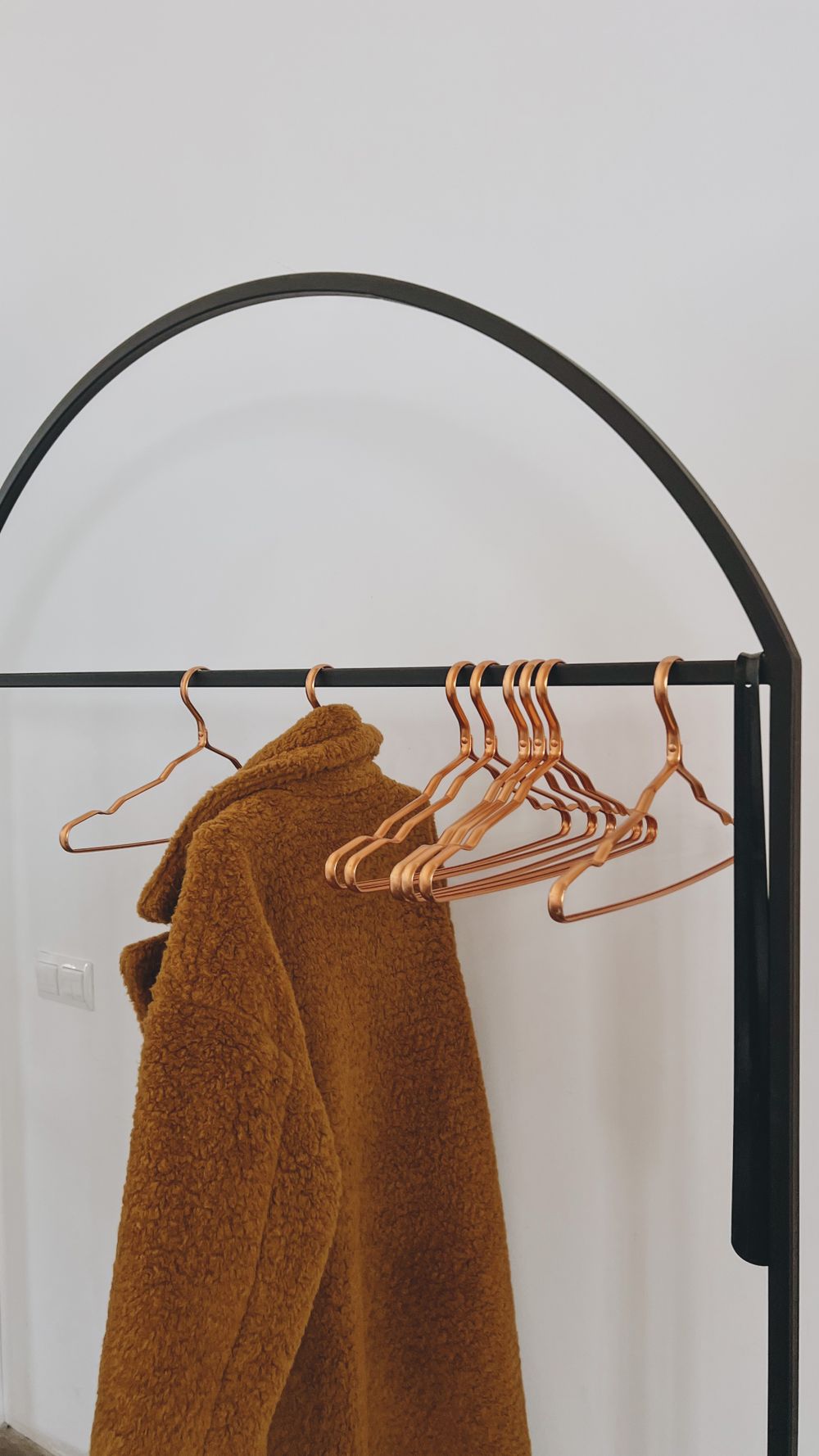 A brown coat hangs on minimalist black clothing rack with empty wooden hangers.
