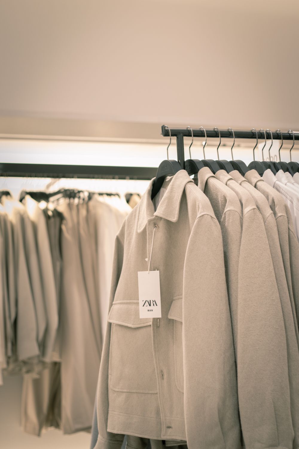 Stylish beige coats neatly arranged on racks in a modern clothing store interior.