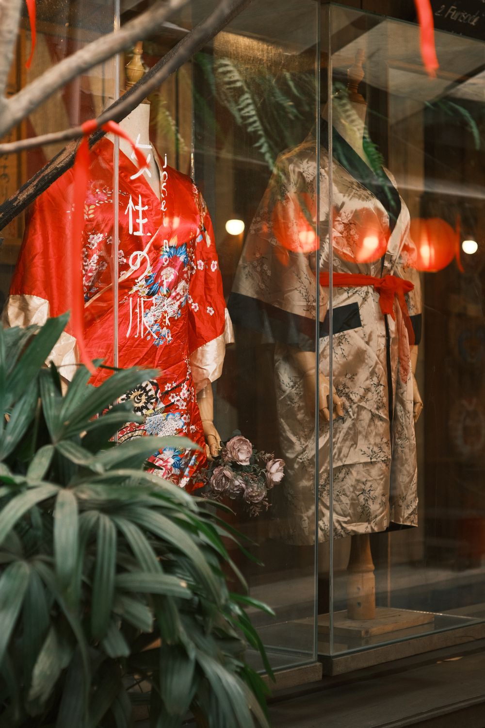 Elegant kimonos featured in a boutique window with vibrant red accents and lush greenery.