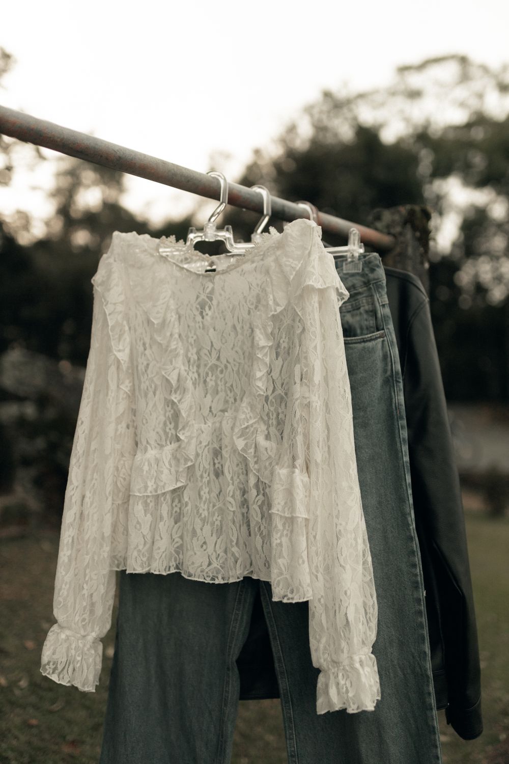An elegant lace blouse and jeans hanging on a clothesline outdoors, creating a chic and relaxed fashion vibe.