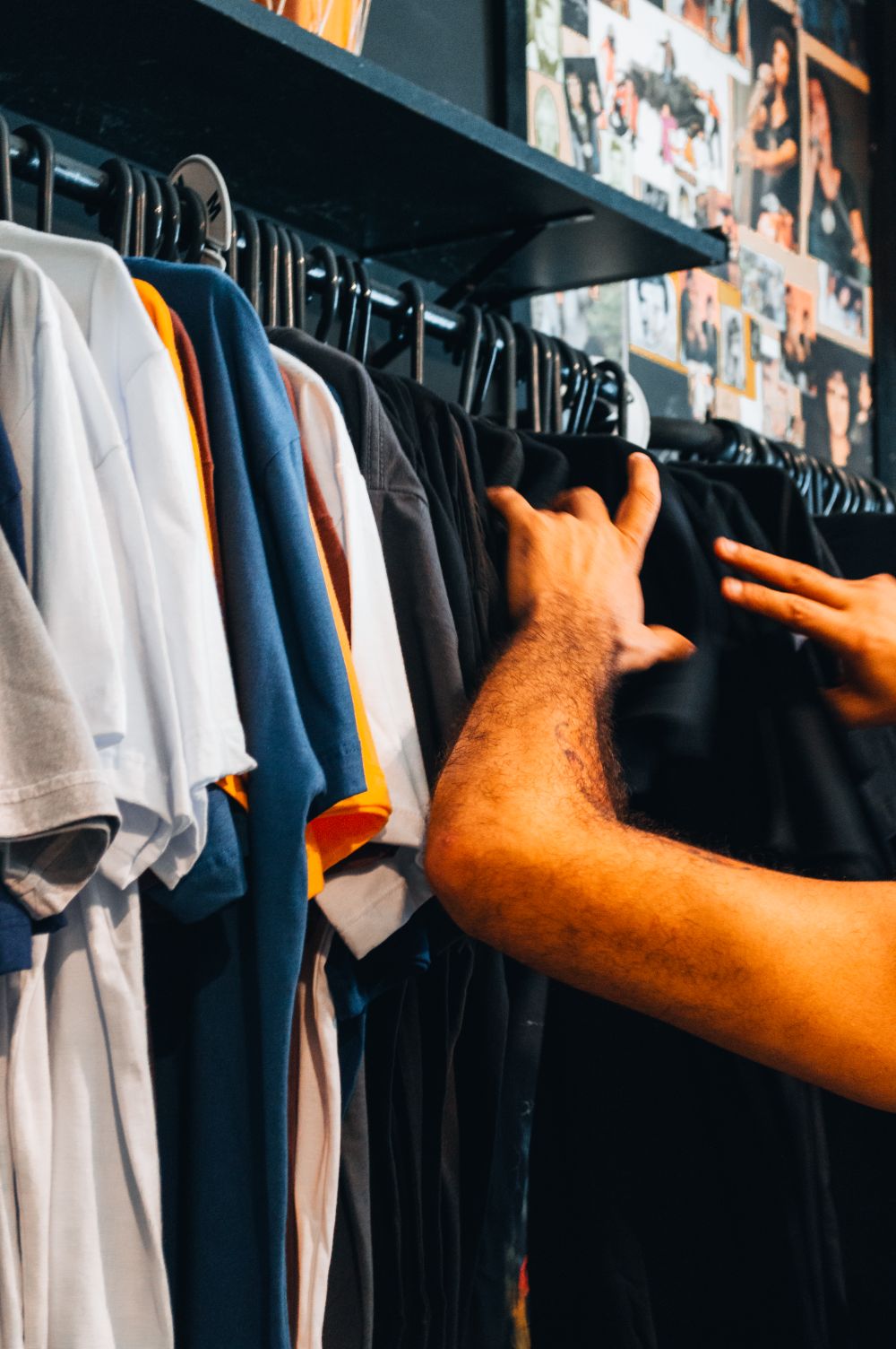 Man browsing colorful T-shirts on a rack in a vibrant clothing store.